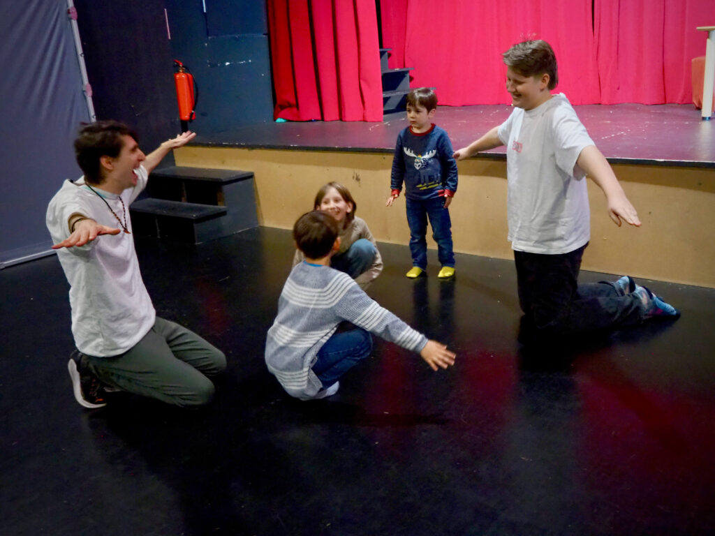 Kinder in Kostümen spielen eine Szene auf der Theaterbühne