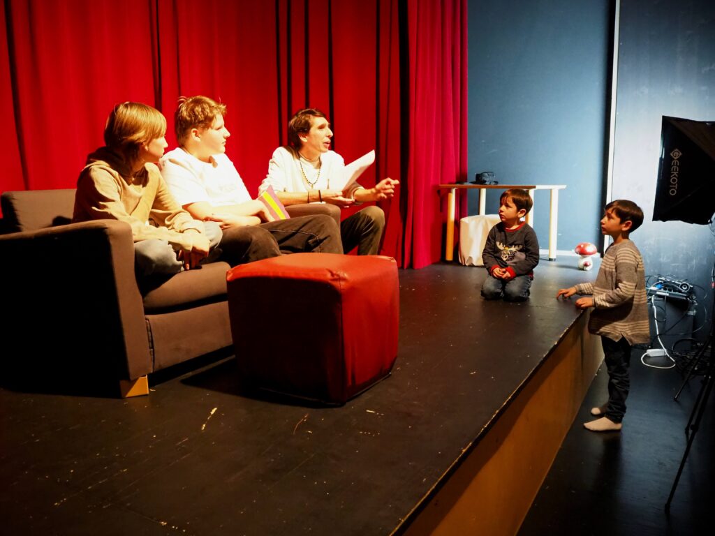 Kinder spielen eine Wohnzimmerszene auf der Theaterbühne