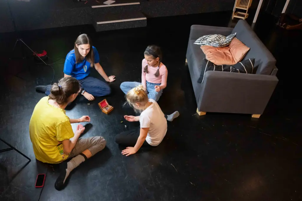 Kinder sitzen im Kreis auf dem Boden und spielen im Theaterkurs